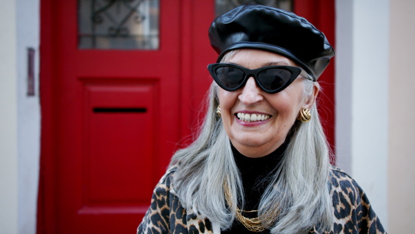 Senior chic woman with sunglasses standing outdoors in town, looking at camera.