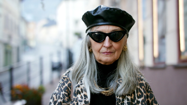 Senior chic woman with sunglasses standing outdoors in town, looking at camera.