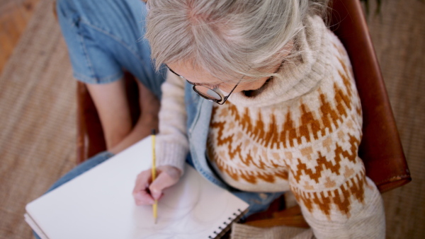 Top view of senior woman designer sitting on floor and drawing on paper.