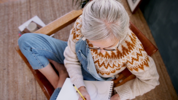 Top view of senior woman designer sitting on chair and drawing on paper.