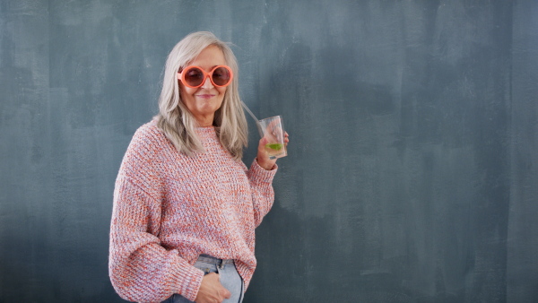 Portrait of senior woman with sunglasses indoors drinking a drink, looking at camera.