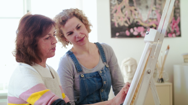 Happy senior woman with teacher or instructor painting pictures in art class.