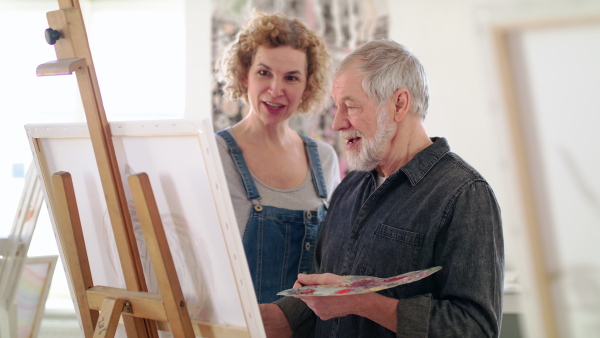 Happy senior man with teacher or instructor painting pictures in art class.