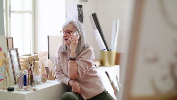 Senior woman or teacher with smartphone making phone call in art class.