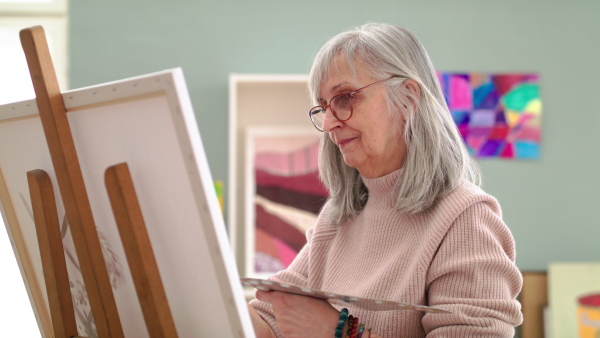 Senior woman with palette painting pictures on canvas in art class. Slow motion.