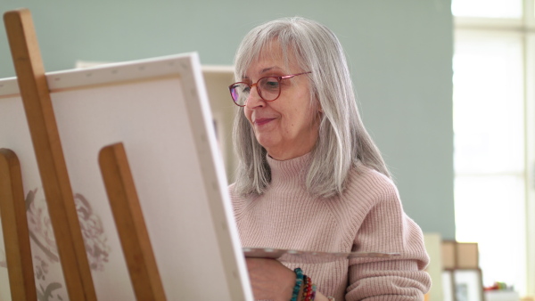 Senior woman with palette painting pictures on canvas in art class. Slow motion.