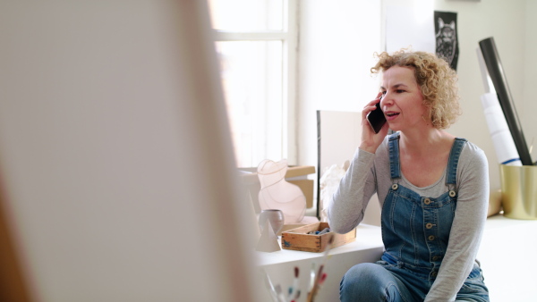 Mature woman or teacher with smartphone making phone call in art class.