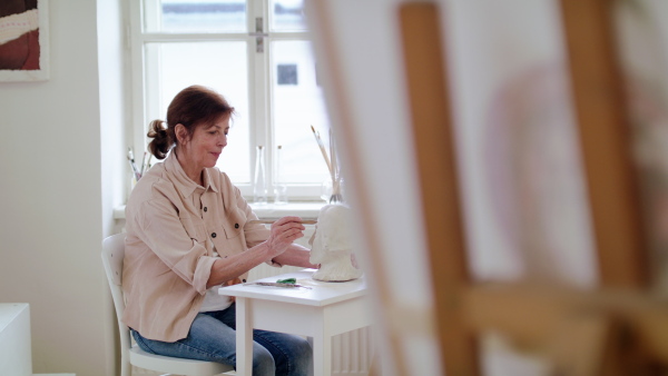 Happy senior woman working on clay head on ceramics workshop.