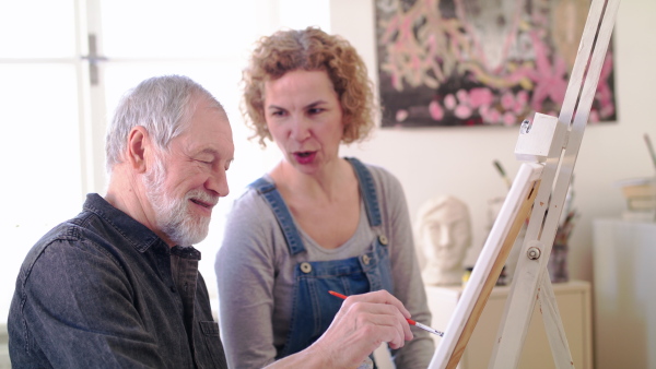 Happy senior man with teacher or instructor painting pictures in art class.