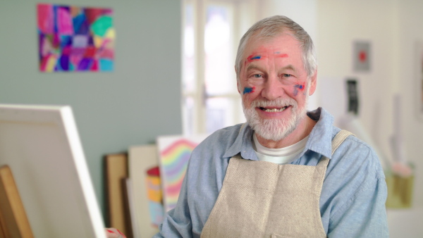 Front view of senior man painting pictures in art class, looking at camera.