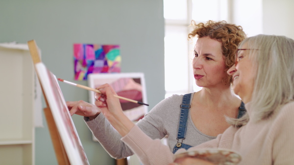 Happy senior woman with teacher or instructor painting pictures in art class.