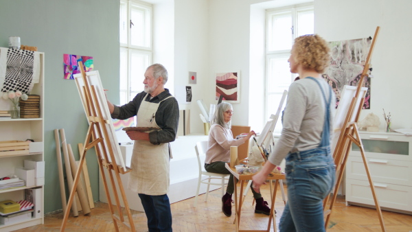 Group of happy senior people with teacher painting pictures in art class.