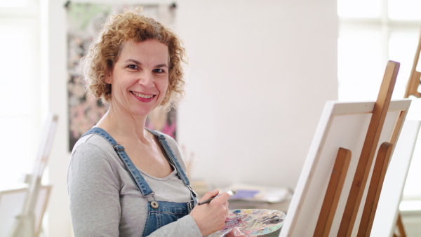 Mature woman with palette painting pictures on canvas in art class.