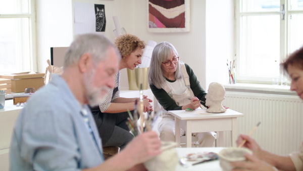 Group of happy senior people with teacher working with clay on ceramics workshop.