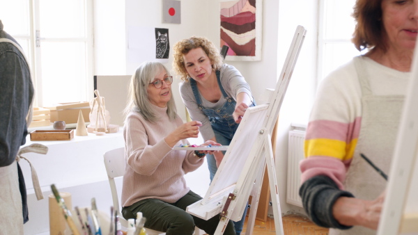 Group of happy senior people with teacher painting pictures in art class.