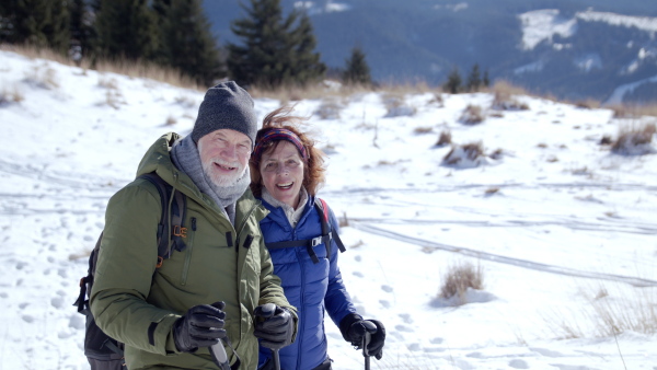 Happy senior couple hikers in snow-covered winter nature, looking at camera.