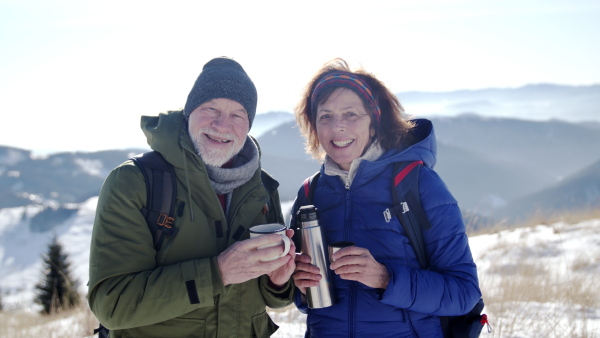 Senior couple hikers resting in snow-covered winter nature, drinking hot tea.