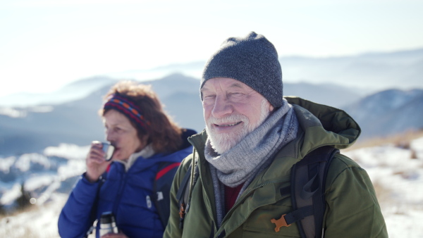 Happy senior couple hikers in snow-covered winter nature, looking at camera.