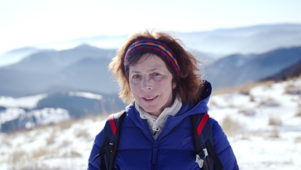 Portrait of senior woman hiker standing in snow-covered winter nature, looking at camera.