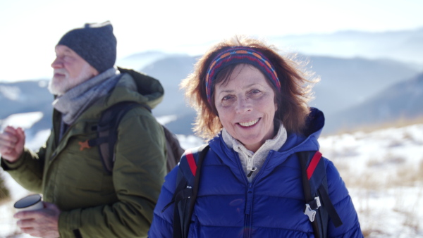 Happy senior couple hikers in snow-covered winter nature, looking at camera.