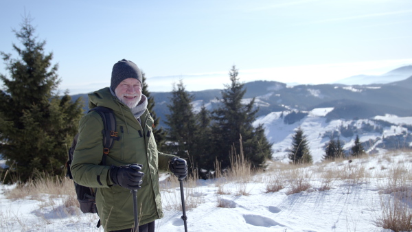 Front view portrait of senior man standing in snow-covered winter nature, looking at camera.