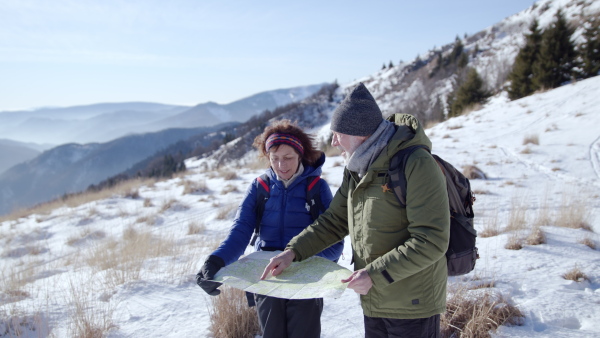 Portrait of senior couple hikers using map in snow-covered winter nature.