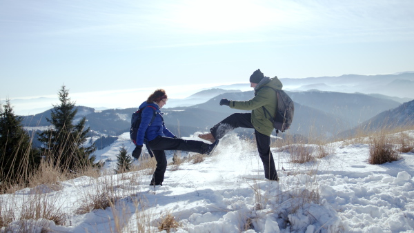 Side view portrait of senior couple hikers standing in snow-covered winter nature, feeling excited.