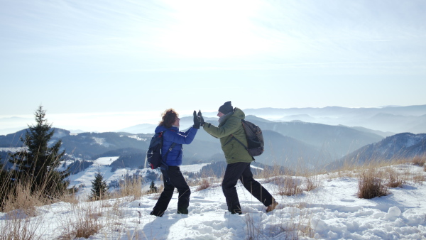 Side view portrait of senior couple hikers standing in snow-covered winter nature, feeling excited.