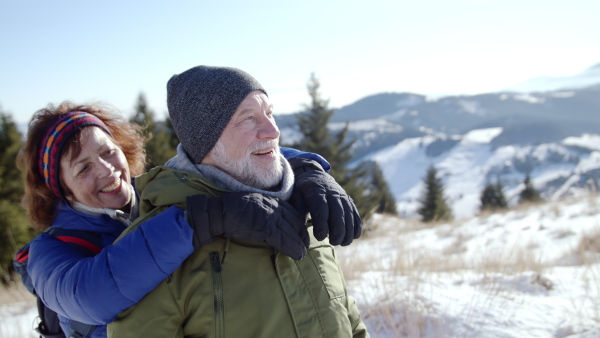 Portrait of happy senior couple hikers standing in snow-covered winter nature, resting.