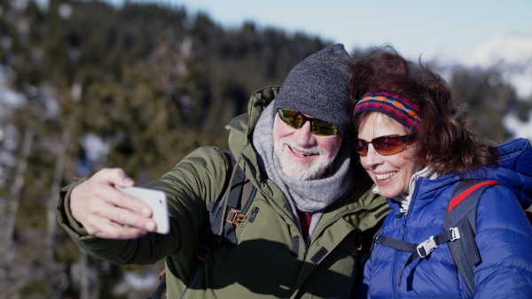 Portrait of senior couple hikers standing in snow-covered winter nature, taking selfie.