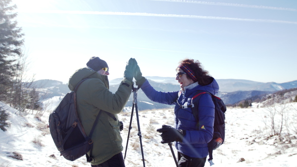 Side view portrait of senior couple hikers standing in snow-covered winter nature, feeling excited.