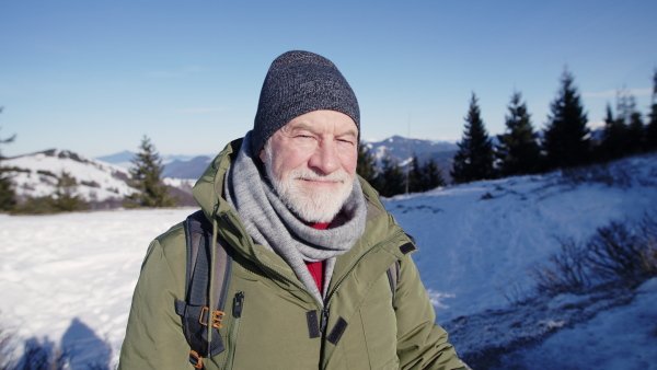 Front view portrait of senior man standing in snow-covered winter nature, looking at camera.