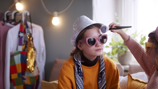 Small sisters indoors at home with sunglasses, applying make-up. Lockdown concept.