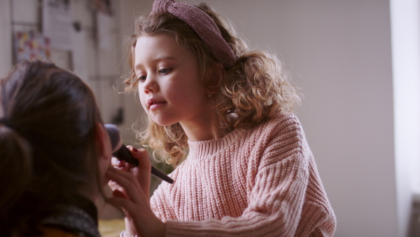 Small sisters indoors at home, applying make-up. Lockdown concept.