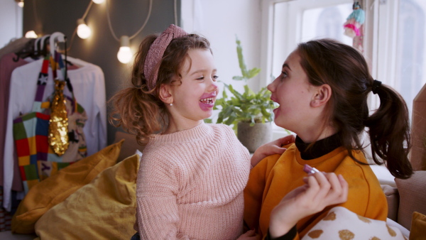 Happy sisters indoors at home, applying lipstick. Lockdown concept.