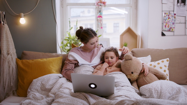 Portrait of sisters indoors at home, using laptop. Lockdown concept.