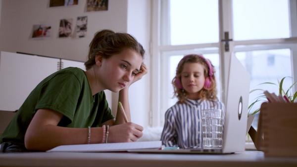 Teenager schoolgirl with sister nexto to her learning online indoors at home, coronavirus concept.