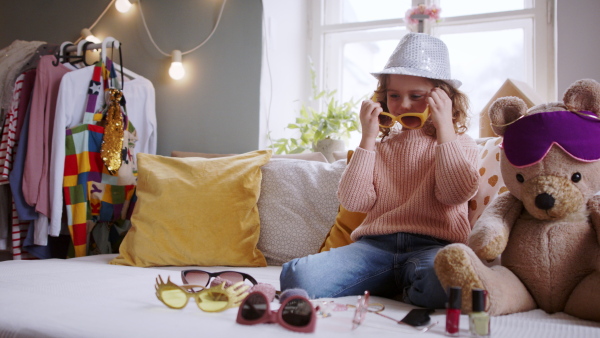 Portrait of small girl indoors at home, playing and dressing up on bed. Lockdown concept.