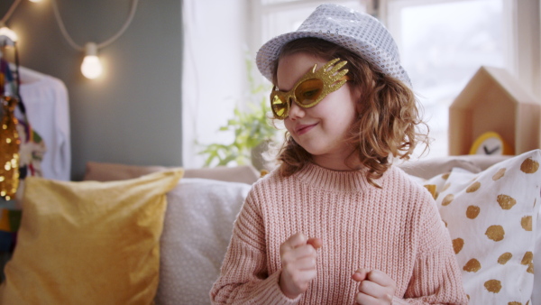 Portrait of small girl indoors at home, playing and dancing on bed. Lockdown concept.