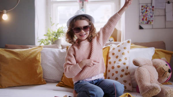 Portrait of small girl indoors at home, playing and dancing on bed, looking at camera. Lockdown concept.