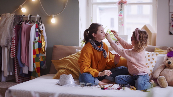 Portrait of sisters indoors at home, playing on bed. Lockdown concept.