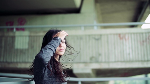 Beautiful young woman with smartwatch standing under the bridge in the city. Slow motion.