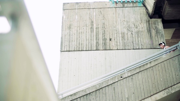 Young athlete with headphones running down the stairs under the bridge in the city. Slow motion.