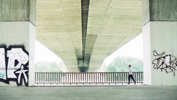 Young athlete man running under the concrete bridge in the city. Slow motion.