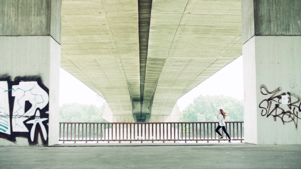 Young athlete woman running under the concrete bridge in the city. Slow motion.