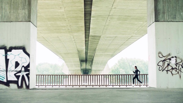 Young athlete woman running under the concrete bridge in the city. Slow motion.