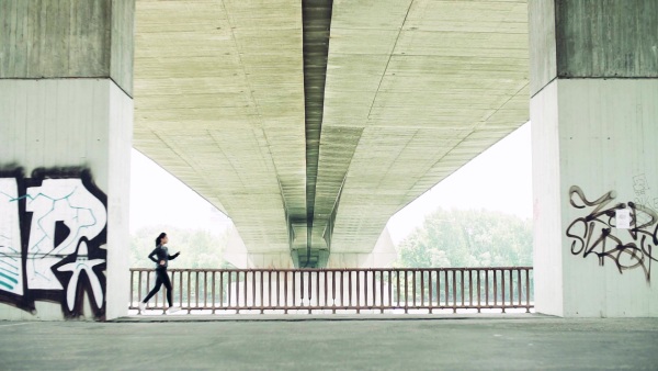 Young athlete couple running under the concrete bridge in the city. Slow motion.