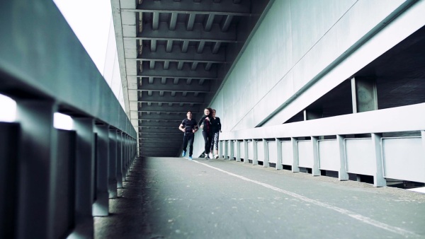 Young athlete friends running under the concrete bridge in the city. Slow motion.