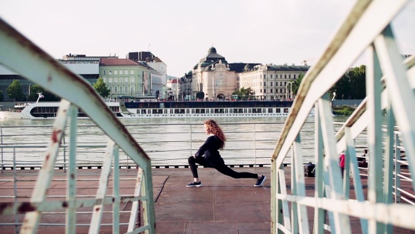 Beautiful young woman stretching outside by the river in the city. Slow motion.