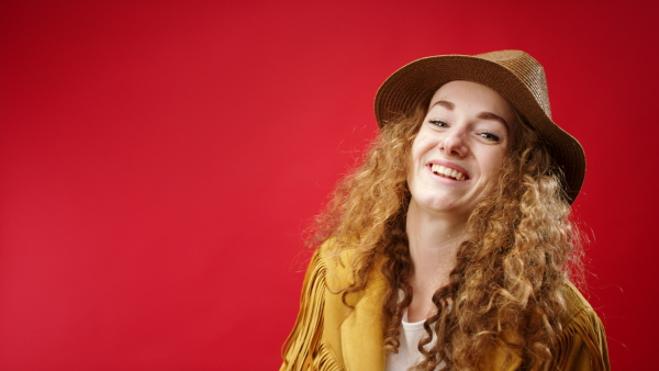 Young woman with hat and balloons in a studio on red background, looking at camera.